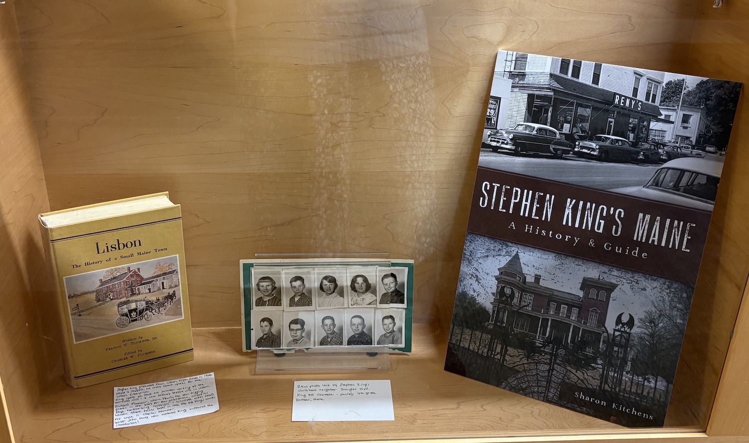 A display case with the book cover of Stephen King's Maine, by Sharon Kitchens, and some class photos