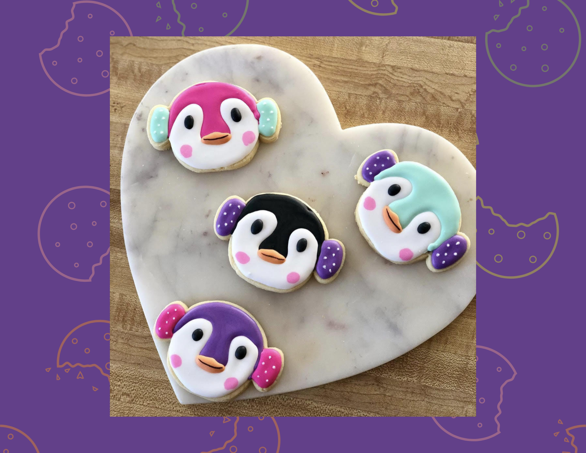 Heart shaped platter with four cookies shaped like penguin faces over purple background