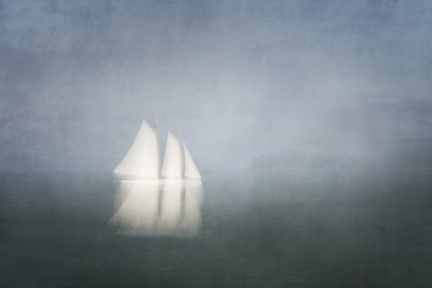 a misty photo of a white sailboat against dark gray water and sky